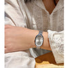 Gros plan d'une femme portant une élégante montre en quartz argent sur son poignet, associée à une manche en dentelle blanche