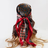 A black and orange patterned satin silk scarf tied around a woman's hair.