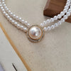 Collier de perles de nacre avec une perle ronde centrale et des strass entourants sur fond clair.