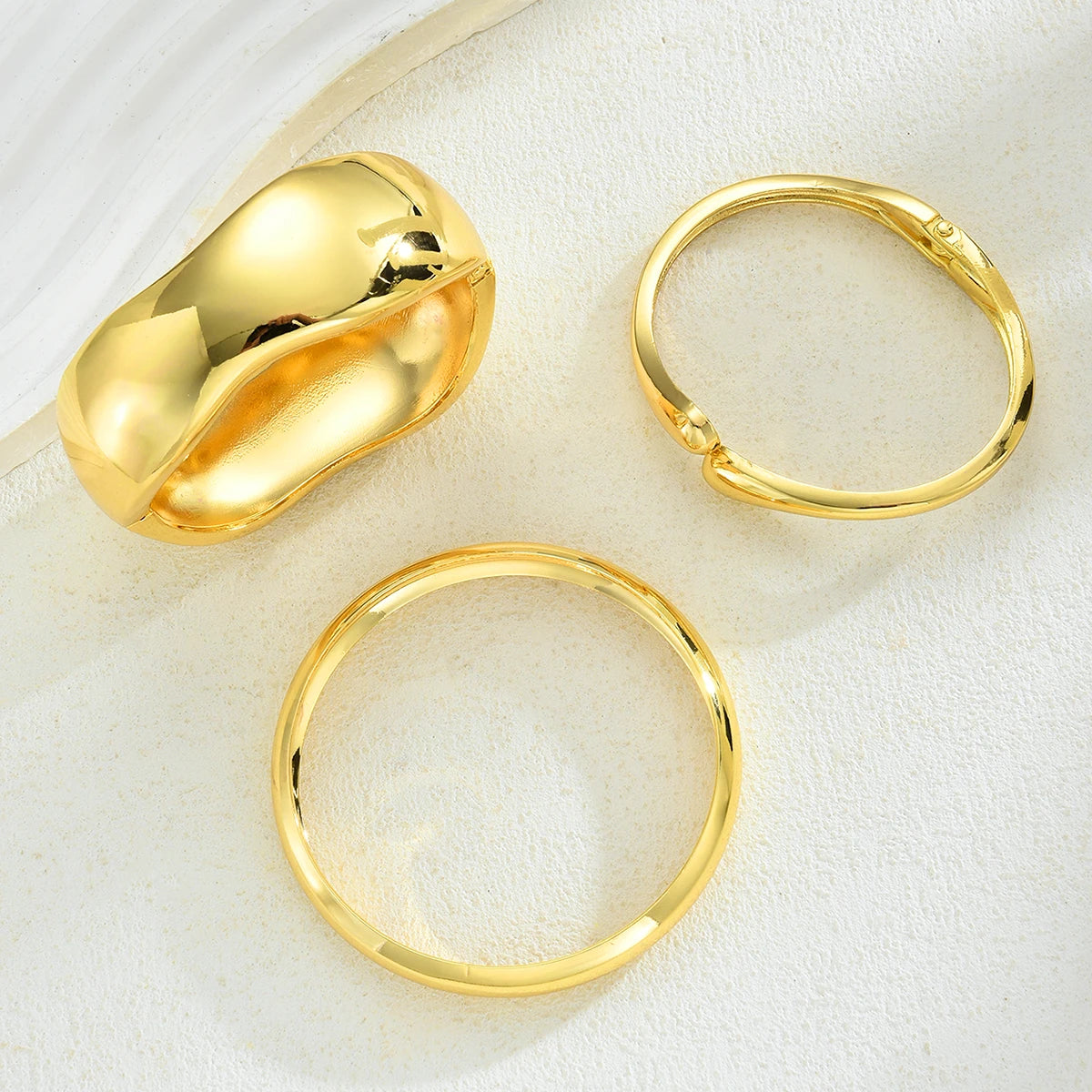 A set of three gold geometric wave bangles, including a large gold claw-shaped piece and two simple gold rings.