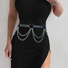 Una mujer vistiendo un vestido negro ajustado con un cinturón de arnés de cuero falso ajustable y cadenas de plata.