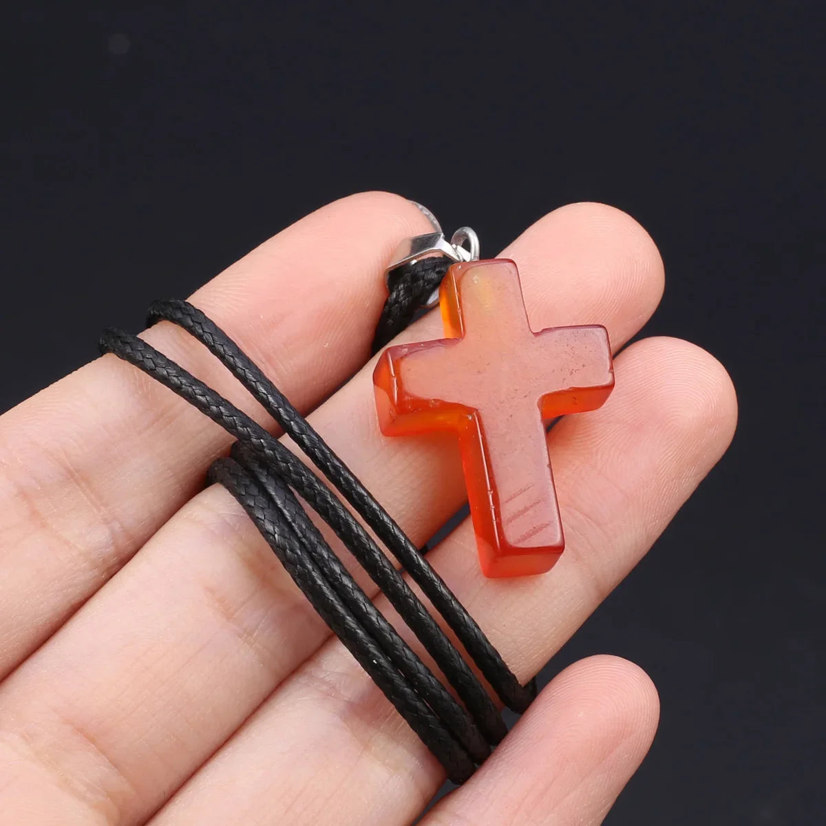 Eine Hand hält eine orange-tigeraugen-Agat-Kreuz-Anhänger-Kette mit einem schwarzen Band.