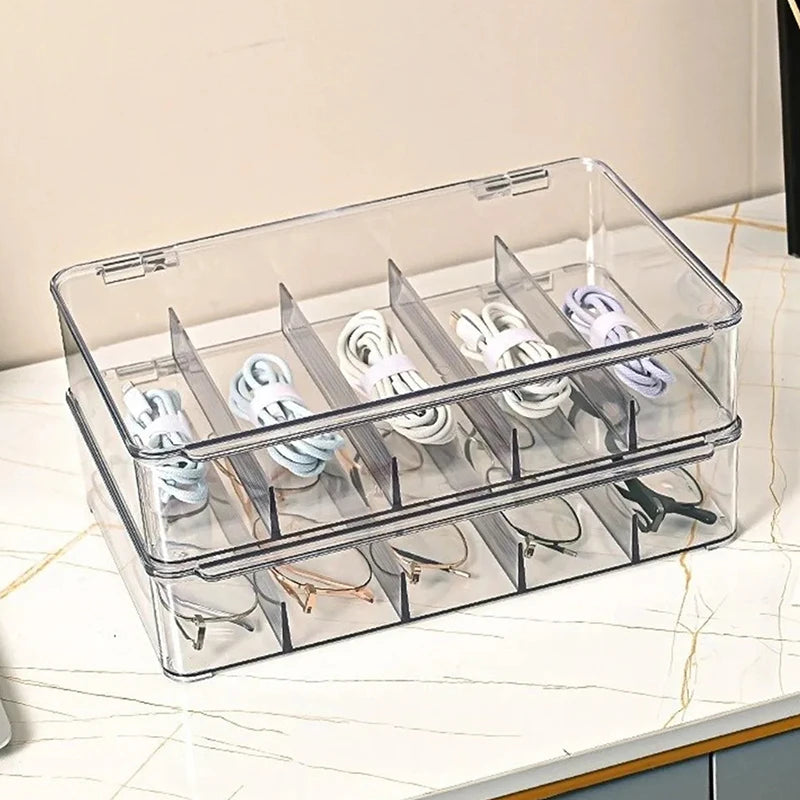 A clear plastic multi-compartment organizer for storing eyeglasses and sunglasses on a white marble surface.