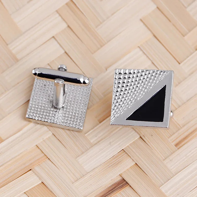 Pince-cuffs carrés argentés avec motif texturé et design triangulaire noir sur un tapis en bambou.