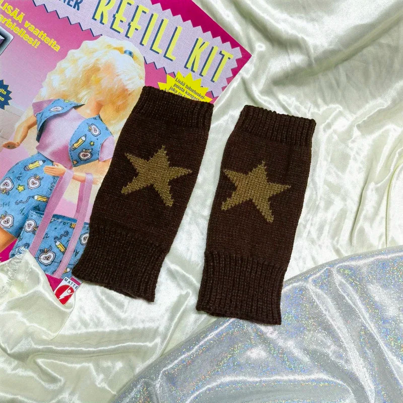 Un par de guantes sin dedos de punto marrón oscuro con diseños de estrella dorada, junto al empaque del producto.