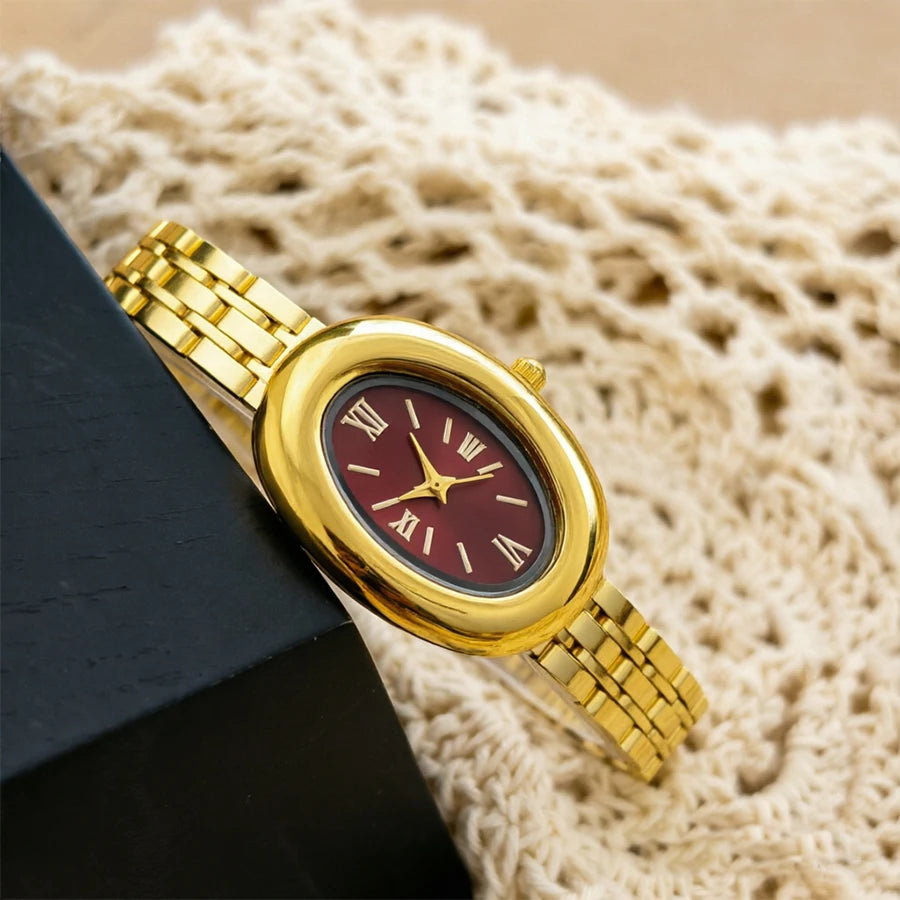 Un reloj estilo vintage con caja y correa dorada descansa sobre tela de punto beige claro.