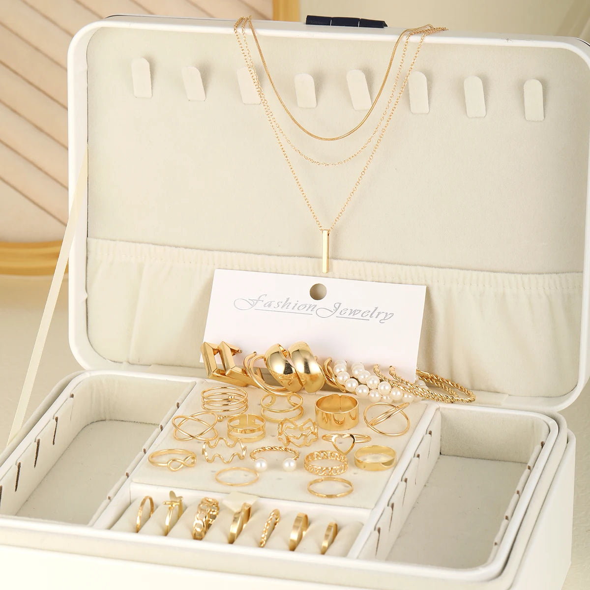 Boîte à bijoux ouverte présentant un ensemble de bijoux géométriques en or et perles, y compris colliers, bagues et boucles d