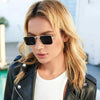 A blonde woman wearing black leather jacket and white top with retro vintage metal frame sunglasses.