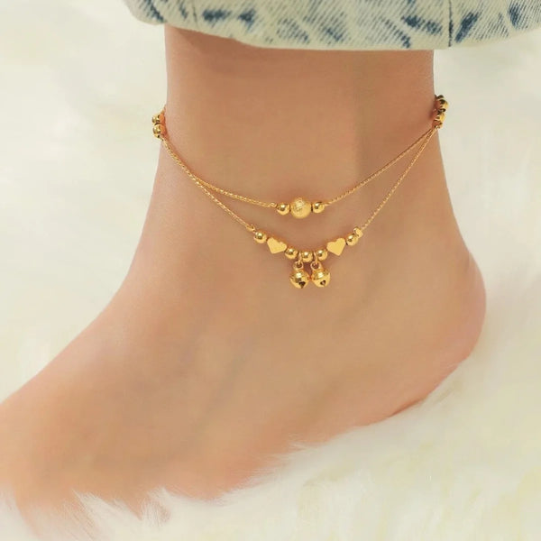 Gold-plated heart bell anklet worn on a woman's ankle against a light background.