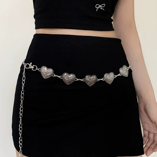 A woman wearing a black skirt and top with a silver heart chain body jewelry accessory.