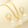 A set of dainty gold pearl jewelry featuring matching earrings and a delicate necklace displayed on a pale yellow background.