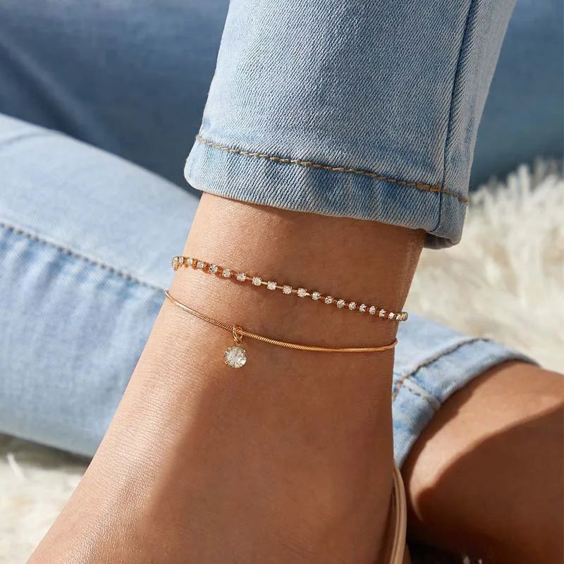A close-up of a woman's wrist wearing an elegant gold geometric anklet bracelet with small diamonds.