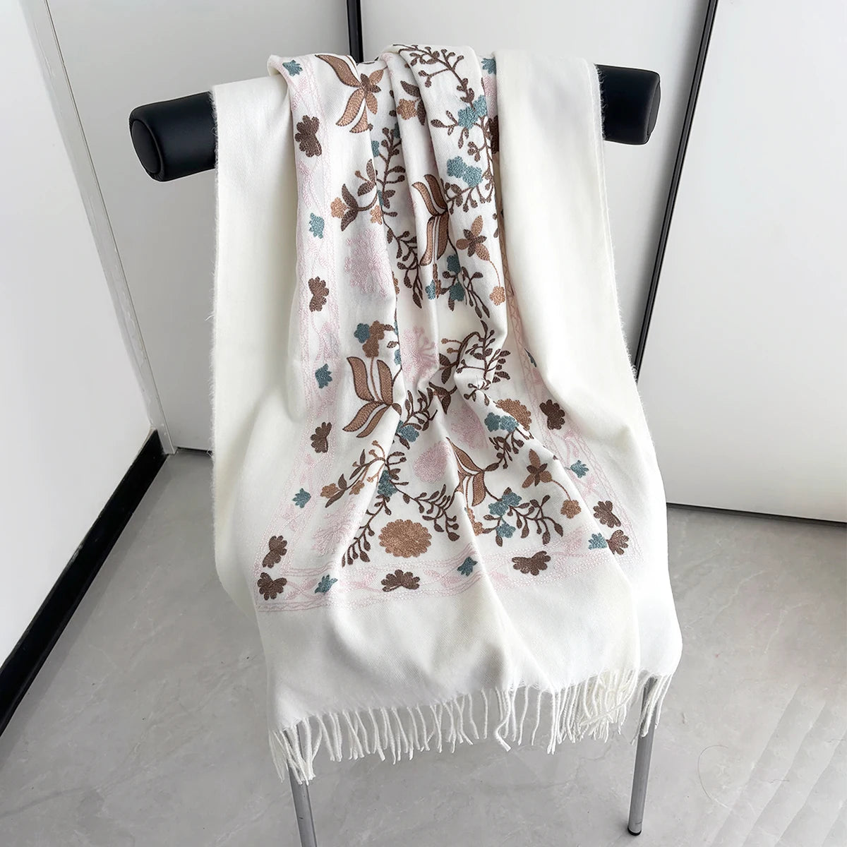 A white luxury floral scarf with brown and blue botanical patterns displayed on a hanger.