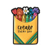 A yellow enamel pin featuring a bouquet of colorful flowers and the text create every day.