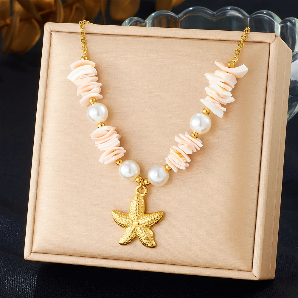 Gold-toned necklace featuring a starfish heart pendant and pink and white floral beads on a light beige box.