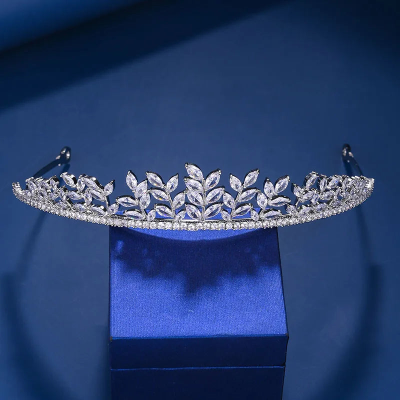 A sparkling cubic zirconia bridal tiara headband displayed on a blue velvet box against a dark blue background.