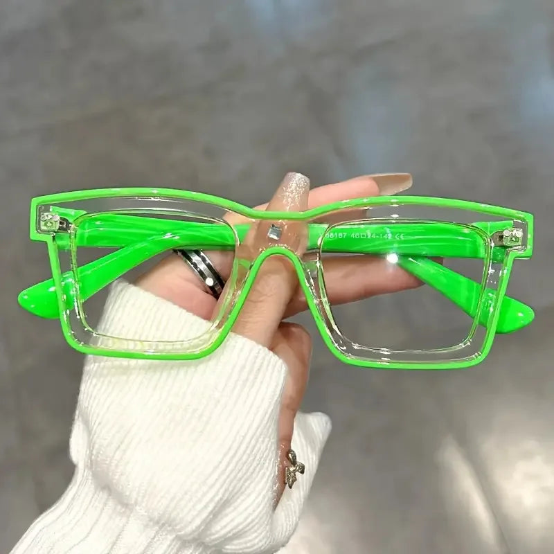 A hand holds a pair of bright green, square-framed costume glasses with clear lenses.