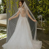 Una novia con vestido de novia blanco y velo de perlas sobre un jardín verde exuberante.