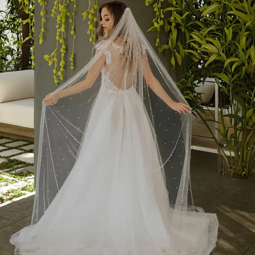 Una novia con vestido de novia blanco y velo de perlas sobre un jardín verde exuberante.