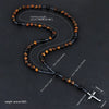 A dark brown and black bead necklace with a hematite cross pendant displayed on a black background.