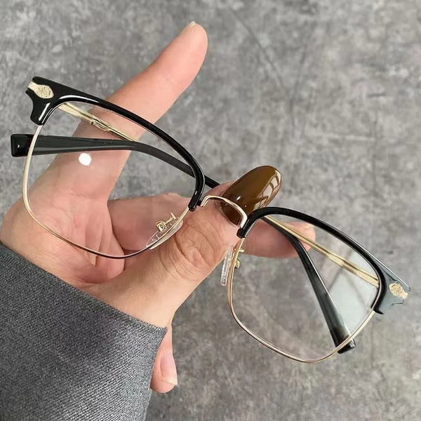 A hand holds a pair of fashion metal half-frame reading glasses with black frames and gold accents.