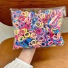 A clear plastic bag filled with colorful, pink, purple, yellow, and blue nylon elastic hair cords.