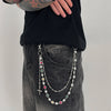 A close-up of a woman wearing a silver pearl cross necklace and matching pendant keychain over dark clothing.
