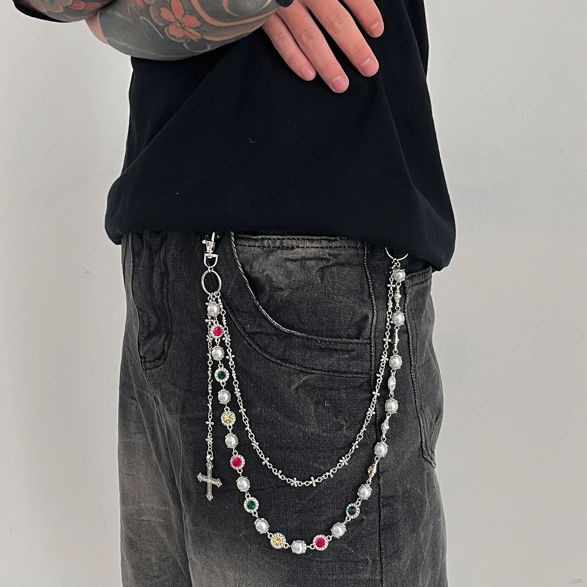 A close-up of a woman wearing a silver pearl cross necklace and matching pendant keychain over dark clothing.