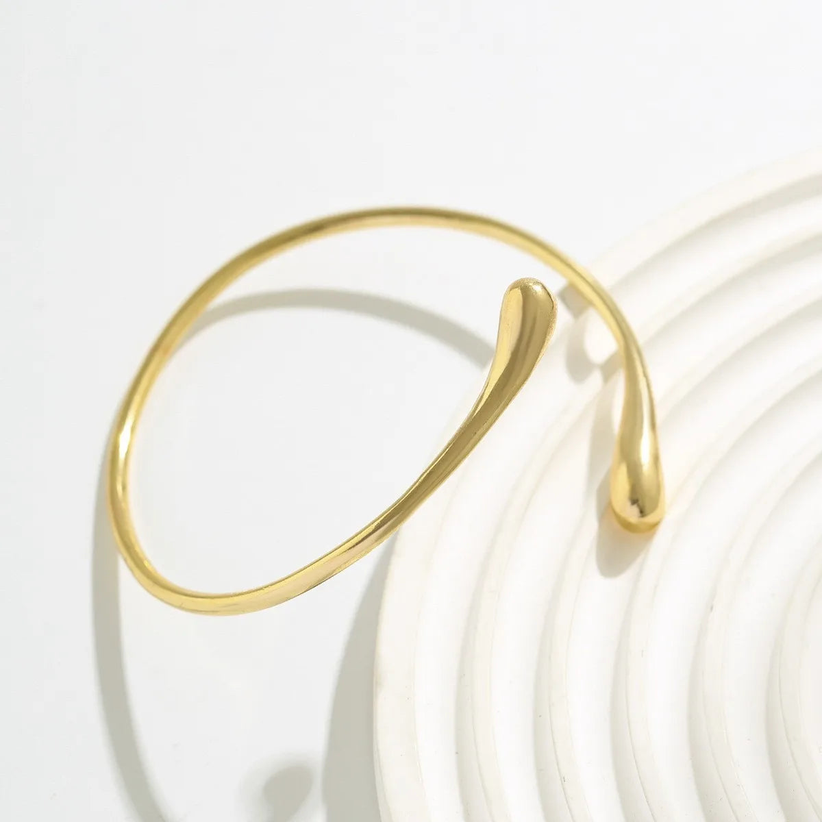 A close-up of a gold droplet arm bangle with an adjustable hook, resting on a white background.