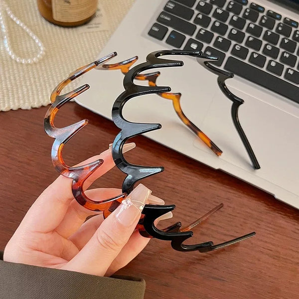 A hand holds a brown resin wave toothed headband with black accents against a white laptop.