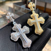 Un collier pendentif en croix serti d'or et d'argent, présenté sur un gant noir.