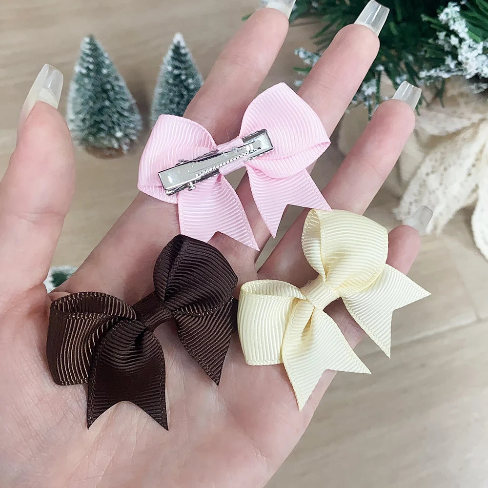 Una mano muestra un juego de tres clips para el pelo de niños de colores sólidos: rosa, marrón oscuro y amarillo pálido.