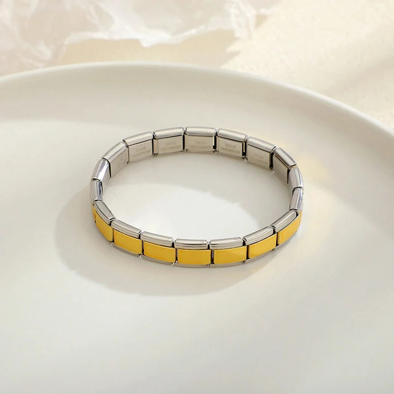 A silver stainless steel charm bracelet with gold accents displayed on a white plate.