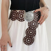 A woman models a vintage western denim belt adorned with silver and brown studs on a white skirt.