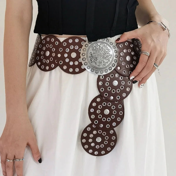 A woman models a vintage western denim belt adorned with silver and brown studs on a white skirt.