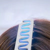 A white hair comb with blue light is shown being used on dark brown hair.