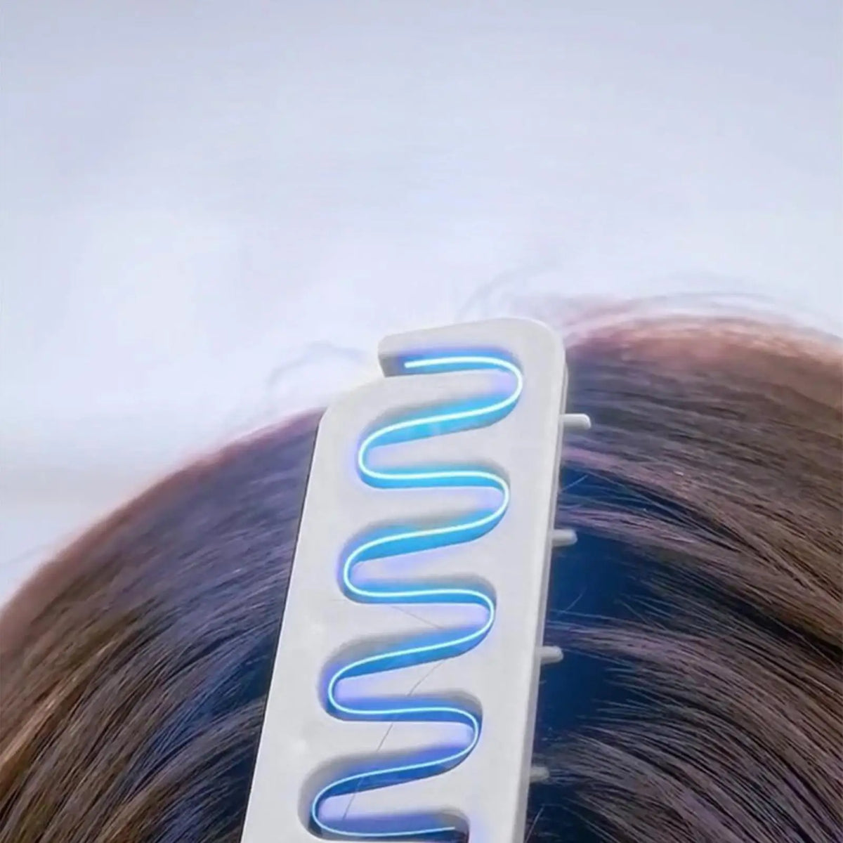 A white hair comb with blue light is shown being used on dark brown hair.
