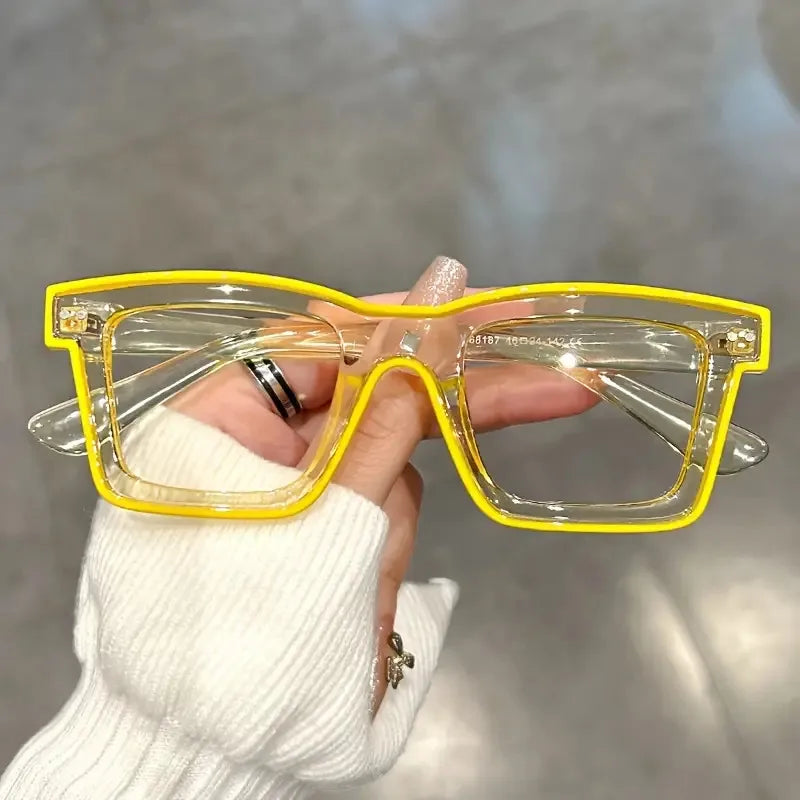 A hand holds a pair of yellow-framed costume glasses with clear lenses against a light background.