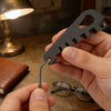 A hand holds a black precision tool used for adjusting eyeglasses, resting near a leather case and glasses.