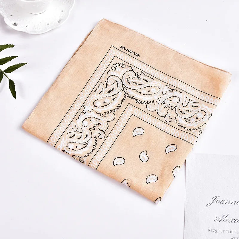 A beige bandana featuring a black bohemian print design is laid diagonally on a white surface.