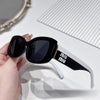 A hand holds a pair of black and white polarized fashion sunglasses against a striped background.