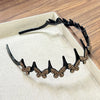 A black headband adorned with sparkling gold butterfly clips is displayed in a light-colored box.