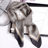 A black and beige plaid silk scarf tied in a knot, displayed on a black tray.