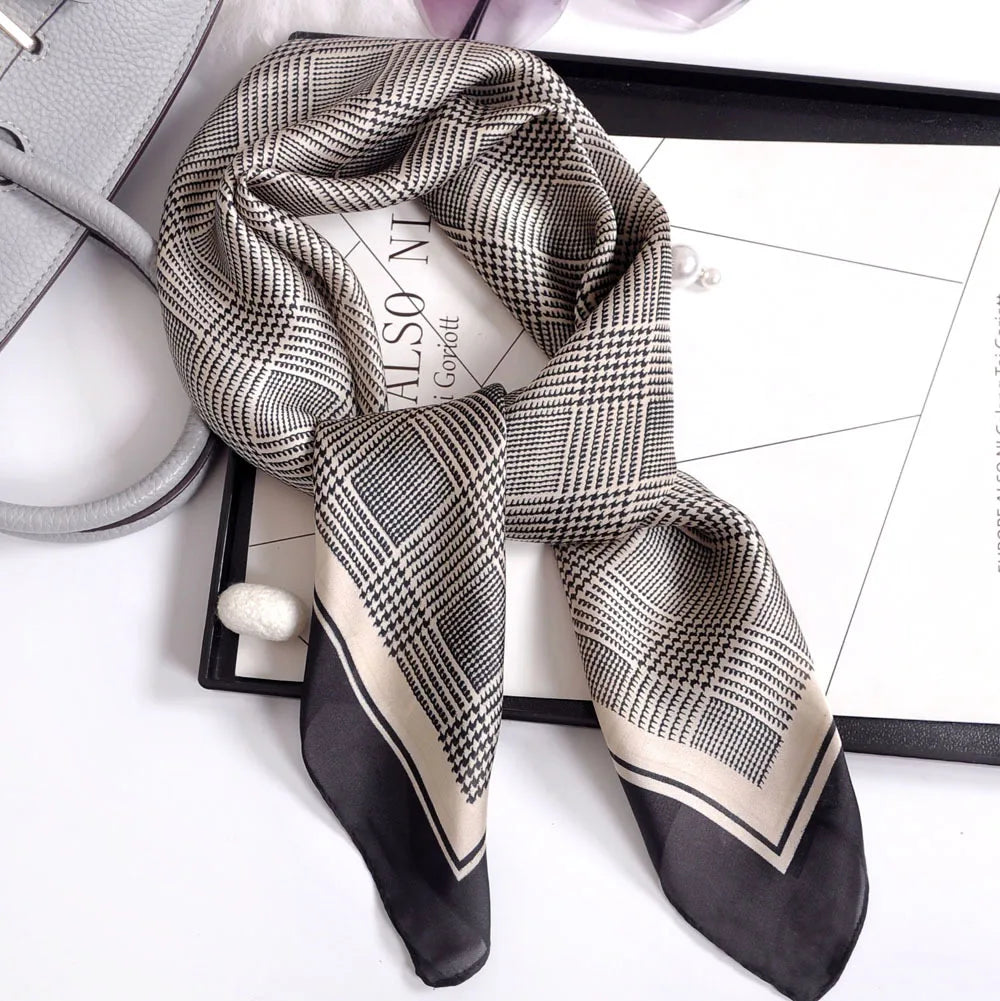 A black and beige plaid silk scarf tied in a knot, displayed on a black tray.