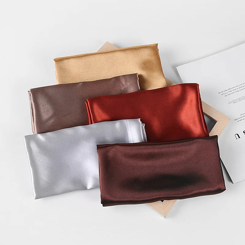 Colección de pañuelos de seda satinada doblados en tonos beige, rojo óxido, plata y marrón oscuro.