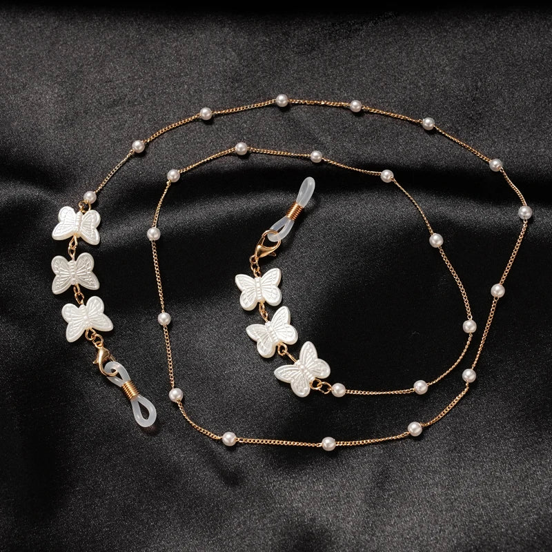 Goldkette mit weißen Schmetterlings- und Perlenanhängern auf dunklem Hintergrund
