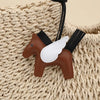 A brown horse pendant charm with white wings attached to a black strap, resting on a cream-colored knitted fabric.