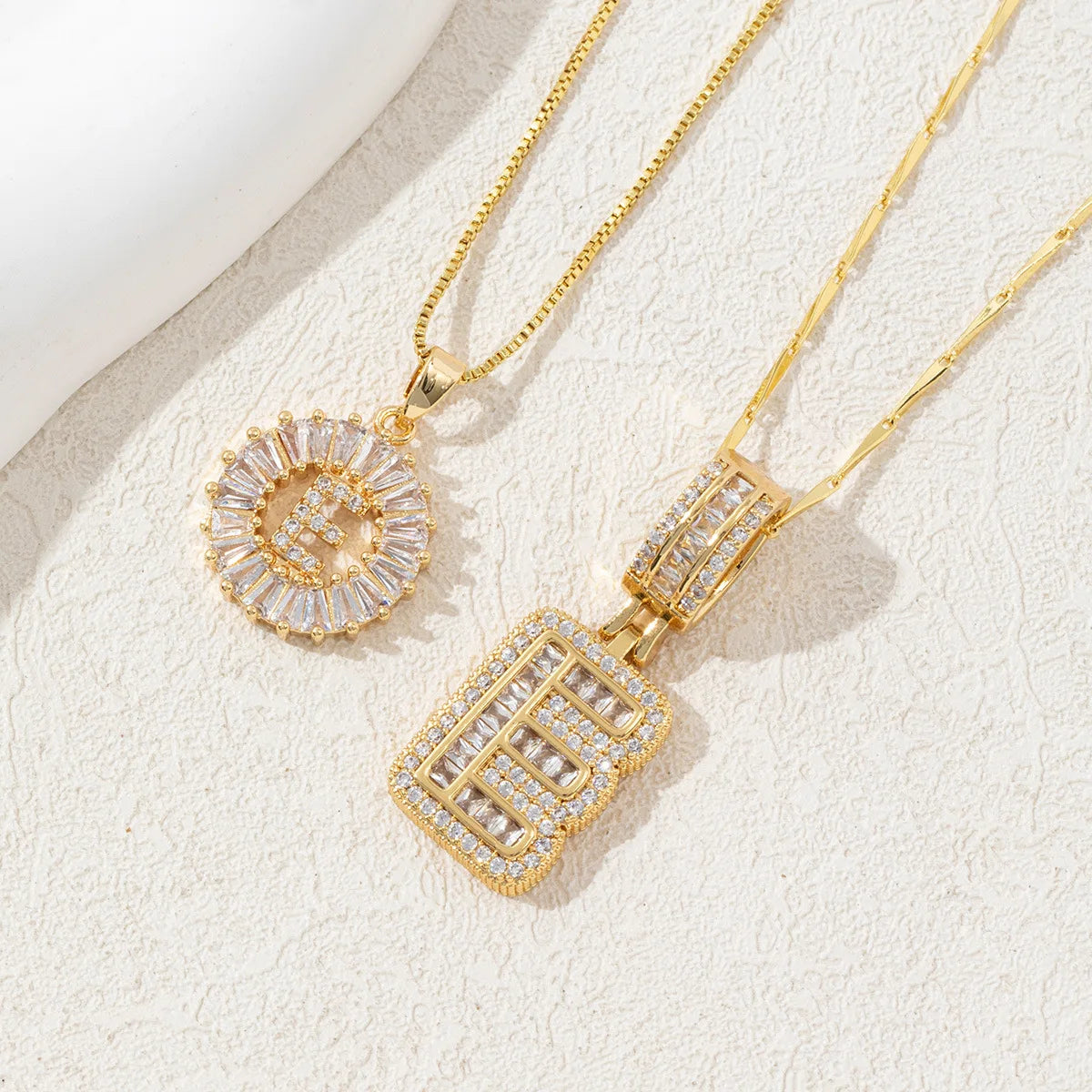 Gold-toned necklace set featuring crystal pendants shaped like the letter E and a diamond-cut square.