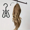 A bundle of long, wavy blonde hair is hanging from a wooden hanger, next to a black wig and accessory hanger.