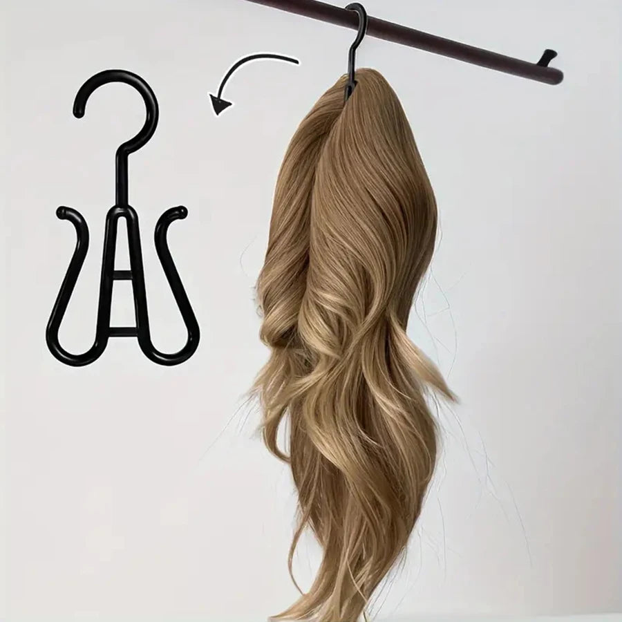 A bundle of long, wavy blonde hair is hanging from a wooden hanger, next to a black wig and accessory hanger.